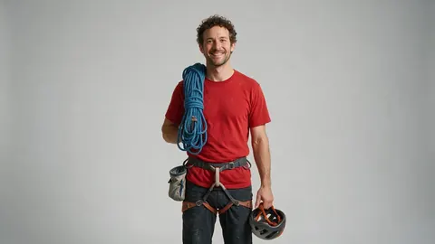 Photo of a climber with a rope, chalk bag and helmet against a grey backdrop (before)