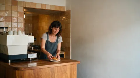 A woman plating a pastry at a small café counter with plain wall space on the right