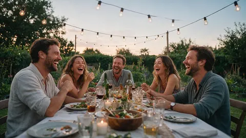 Five friends laughing around a long outdoor dinner table under string lights at dusk
