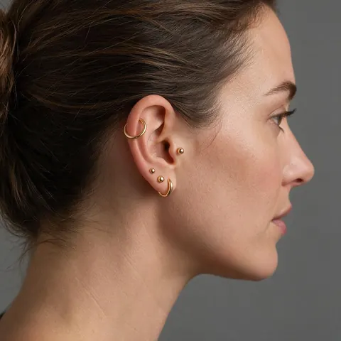 Woman in her 30s with several gold ear piercings