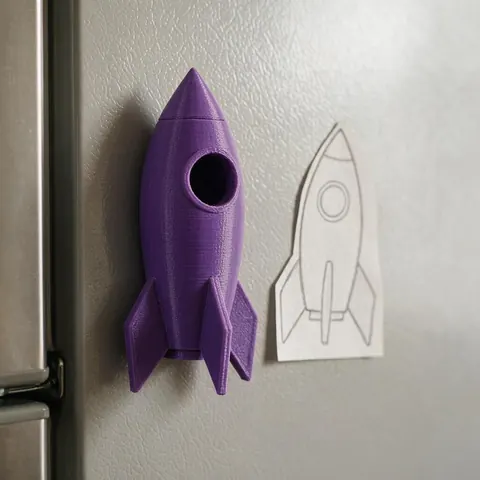 3D printed rocket shape magnet beside the paper drawing on a fridge