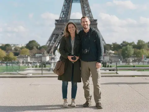 Couple at the Eiffel Tower with a stranger in a red jacket walking behind them