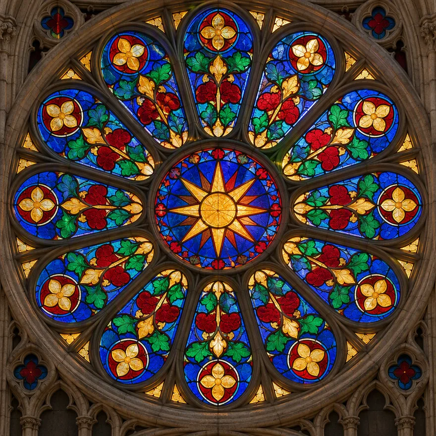 A circular cathedral rose window in stained glass with radial symmetry, a golden starburst center and cobalt, ruby, amber and emerald panes in gothic stone tracery