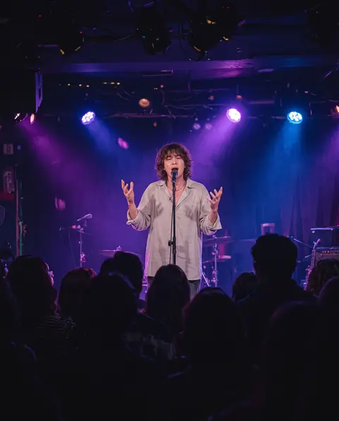 Singer on a small club stage under purple and blue lights