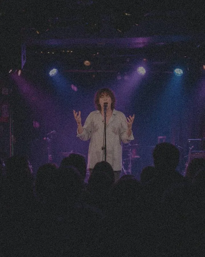 Singer on a small club stage under purple and blue lights — original 720 px, heavy noise