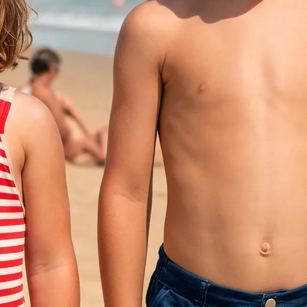 Faded 1970s colour snapshot of two children on a beach with a red-magenta cast — the same crop after Phota Enhance